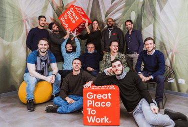 happy tiko italia team standing and sitting with two red cubes written great place to work on it